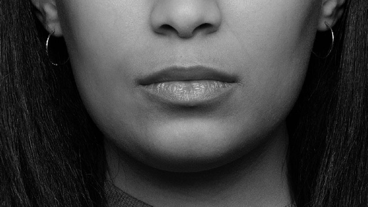 A woman faces directly to the camera in a close up black and white photo of her mouth being the focus of the photo.